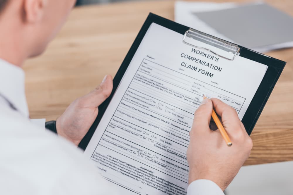 Cropped view of a businessman completing a compensation claim form at his office desk, emphasizing attention to detail and professional documentation.