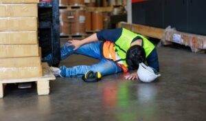 Warehouse Worker Lying on the Floor After an Accident in a Factory. Professional Engineering Team Responding to the Emergency.