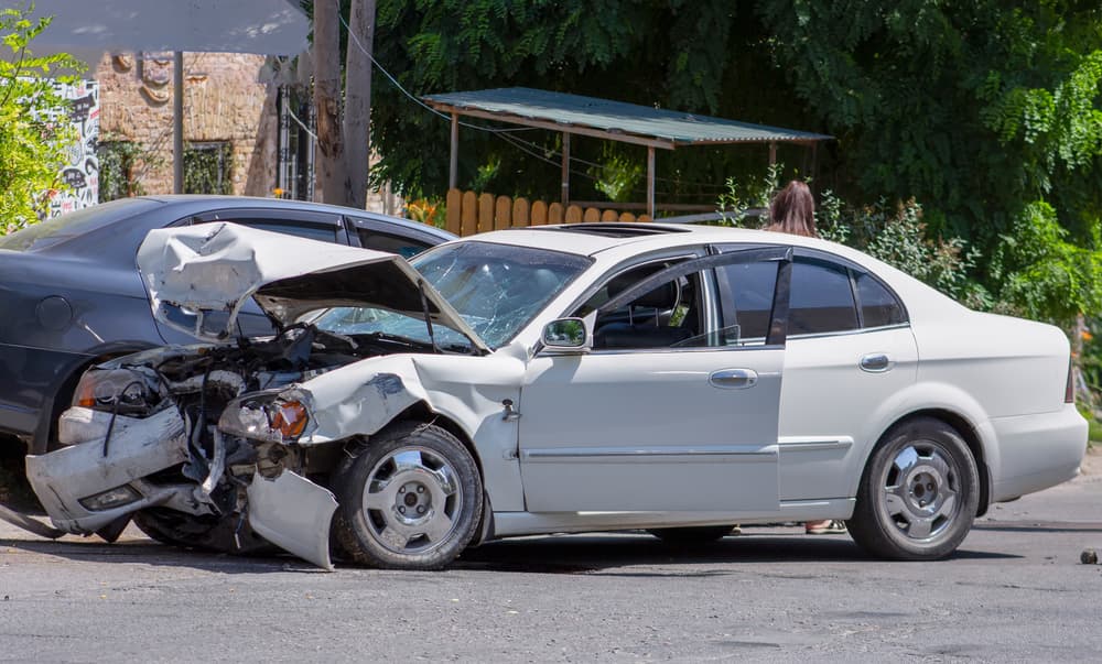 Two cars remain on the road after a collision, with a damaged white car visibly impacted by the accident.







