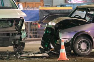 Damaged in heavy car accident vehicles after collision on city street crash site at night.