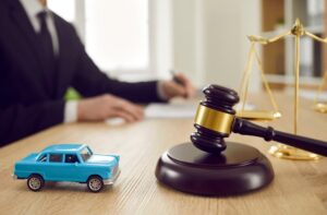 A small toy car and a judge's gavel on a table, with a judge in the background signing a document.