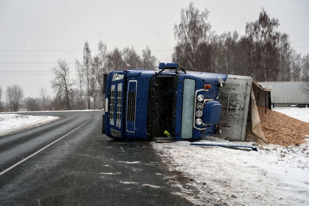 A truck carrying sawdust has overturned on the slippery road.