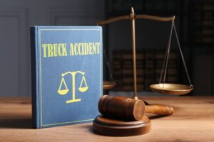 A truck accident law book, a judge's gavel, and scales of justice rest on a wooden table.