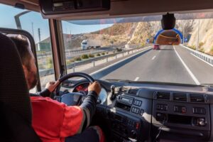 A truck driver, viewed from inside the cab, navigates the highway while approaching a tunnel entrance. 